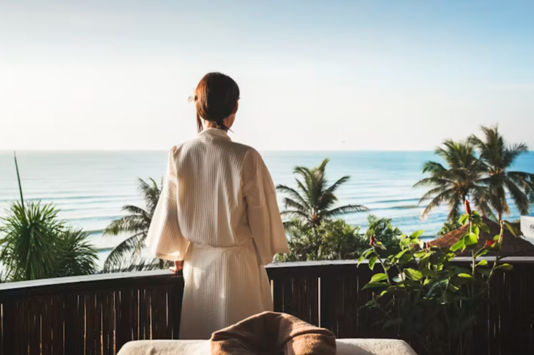 Woman in a robe looking out at the ocean in the morning